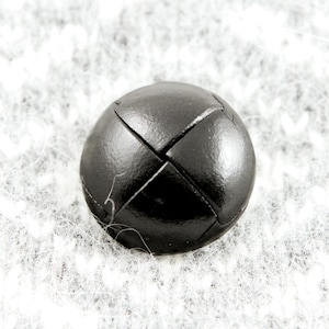 May include: A black leather button with a cross-stitch design.