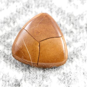 Könnte beinhalten: Ein dreieckiger Lederfleck mit brauner Farbe und einer strukturierten Oberfläche.