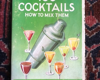 Op de afbeelding: Een vintage groen boek getiteld "100 Cocktails: Hoe ze te mixen" met een cocktailshaker en glazen met kleurrijke drankjes. De omslag van het boek bevat ook de prijs "3'6 NET".