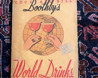以下が含まれることがあります： 「カクテル・ビル・ブースビーの世界の飲み物とその作り方」というタイトルのヴィンテージブック。表紙には、地球儀を背景に、赤い液体の入ったグラスを2つ持つ手の漫画イラストが描かれている。