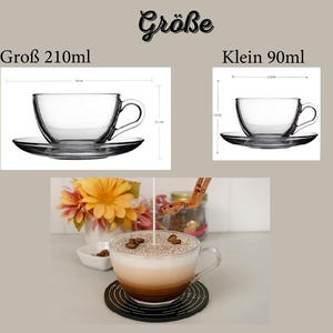 May include: Clear glass teacups and saucers. One cup is labeled as 210ml and the other as 90ml. The image also shows a cup of coffee with foam and coffee beans on top, sitting on a black coaster.