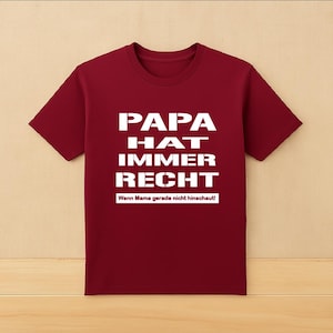 May include: A maroon t-shirt with white text that reads "PAPA HAT IMMER RECHT" in a bold, sans-serif font. Below the main text is smaller text that reads "Wenn Mama gerade nicht hinschaut!"