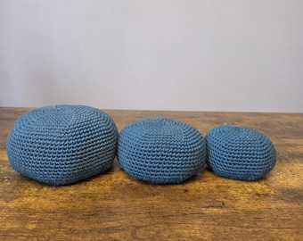 Könnte beinhalten: Drei blaue, gehäkelte Sitzsäcke in verschiedenen Größen sind auf einer Holzoberfläche angeordnet. Die Sitzsäcke haben eine einfarbige, gedämpfte blaue Farbe und ein strukturiertes, gestricktes Aussehen. Die Sitzsäcke sind rund und scheinen mit einem weichen Material gefüllt zu sein.