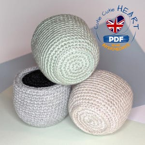 Puede incluir: Tres macetas de crochet en diferentes tonos de gris. Las macetas están apiladas una encima de la otra. La maceta superior es de color verde claro, la maceta del medio es de color gris oscuro y la maceta inferior es de color gris claro. Las macetas son todas redondas y tienen una superficie texturizada.