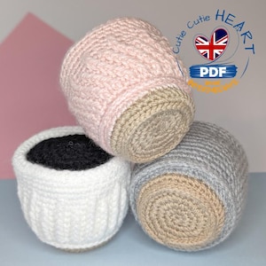 Puede incluir: Tres macetas de ganchillo hechas a mano en colores pastel. Una es blanca con relleno negro, otra rosa claro y la tercera gris. Las bases de las macetas son de color beige. La imagen incluye un logo con el texto "Cute Cutie Heart PDF".