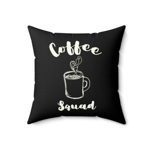 May include: Black throw pillow with white text that reads "Coffee Squad" and a stylized drawing of a coffee mug with steam rising from it.