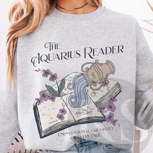 May include: Gray sweatshirt with a graphic of an Aquarius zodiac sign pouring water from a pitcher into an open book. The text "The Aquarius Reader" is above the graphic and "Unconventional Creativity on Every Page" is below the graphic.