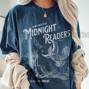 May include: A blue t-shirt with a white graphic design that says "Secret Society of Midnight Readers" with an owl, a crescent moon, a feather, and an hourglass. The text at the bottom says "Best for the Unread."