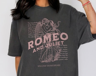 May include: A black t-shirt with a vintage-style graphic print of Romeo and Juliet. The text "ROMEO AND JULIET" is in pink and the text below is in white. The graphic is of a couple embracing with an angel's wings. The text below the graphic reads "WILLIAM SHAKESPEARE".