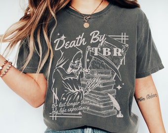 May include: A gray t-shirt with a graphic of a skeleton holding a scythe and a stack of books. The text "Death By TBR" is above the graphic and the text "tbr list longer than my life expectancy" is below the graphic.