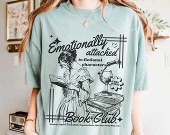 May include: A light blue t-shirt with a black and white illustration of a woman reading a book. The text on the shirt reads "Emotionally attached to fictional characters" and "Book Club".