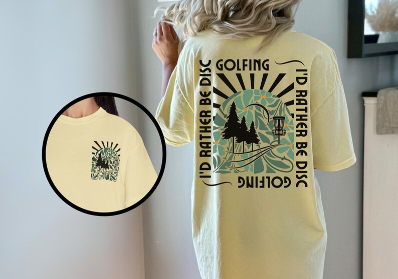 May include: A yellow t-shirt with a graphic design on the back. The design features a disc golf basket, trees, and the text "Golfing I'd rather be disc golfing".
