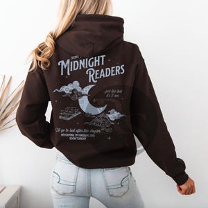 Pu&ograve; includere: Una felpa con cappuccio marrone scuro con la scritta "SECRET MIDNIGHT READERS" e una grafica di luna e nuvole. La felpa ha anche la scritta "...just like that it's 2 am" e "I'll go to bed after this chapter NEVERMIND I'M FINISHING THIS BOOK TONIGHT."