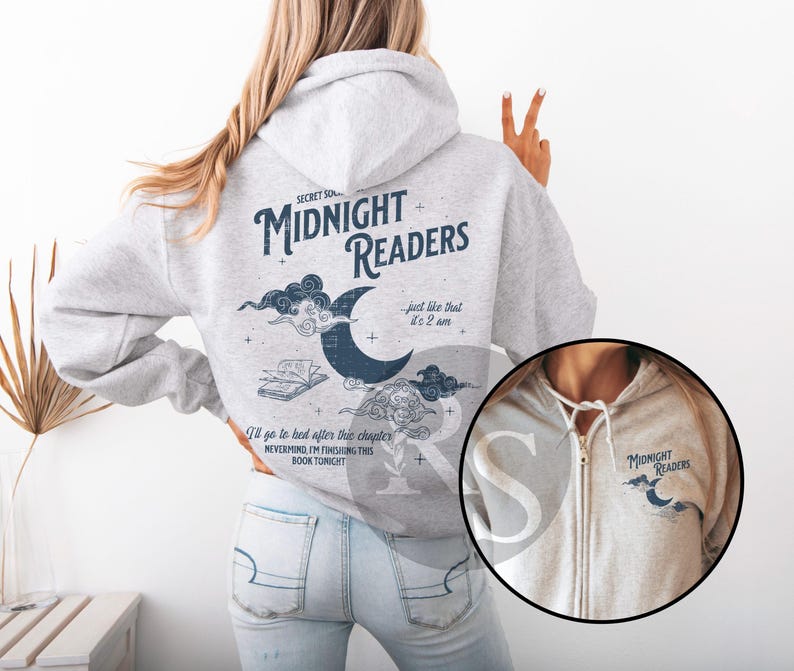 Pu&ograve; includere: Una felpa con cappuccio grigio chiaro con la scritta "MIDNIGHT READERS" e una grafica a mezzaluna. La parte posteriore della felpa ha testo aggiuntivo e una grafica di un libro e nuvole. La parte anteriore ha un piccolo logo.