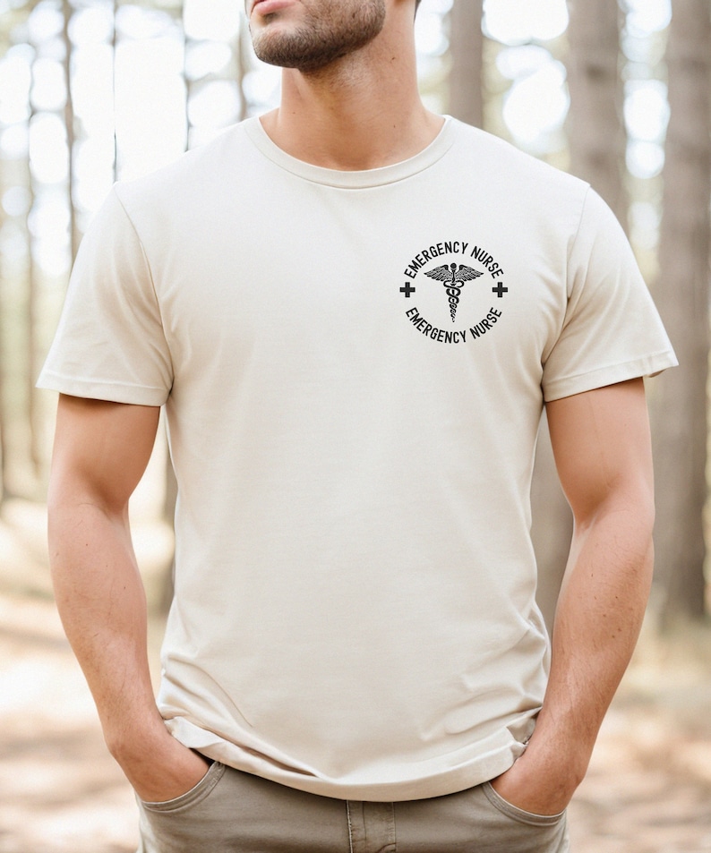 May include: A beige t-shirt with a black graphic of a medical symbol and the text "Emergency Nurse" around it.