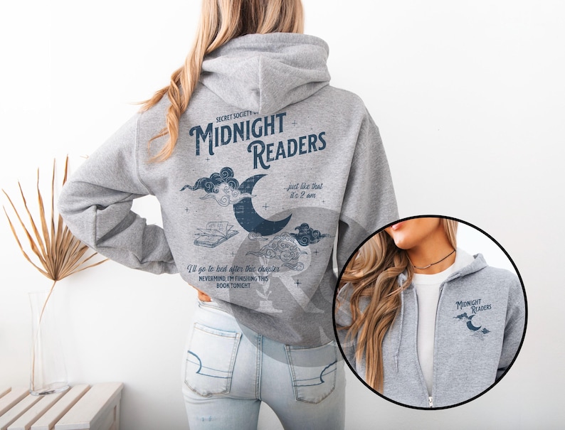 Pu&ograve; includere: Felpa con cappuccio grigia con la scritta "MIDNIGHT READERS" e illustrazioni di una luna crescente, nuvole e un libro. La felpa ha una cerniera e un piccolo logo sul petto.