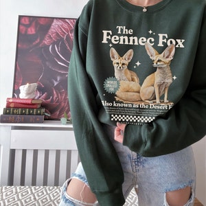 May include: Green sweatshirt with a graphic of two fennec foxes and the text "The Fennec Fox" and "Worlds Smallest Fox". The text "Also known as the Desert Fox" is also included.