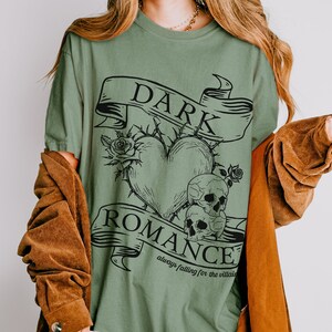 Op de afbeelding: Groen T-shirt met een zwart grafisch ontwerp van een hart met doornen, twee schedels en een banner met de tekst "DARK ROMANCE always falling for the villain".
