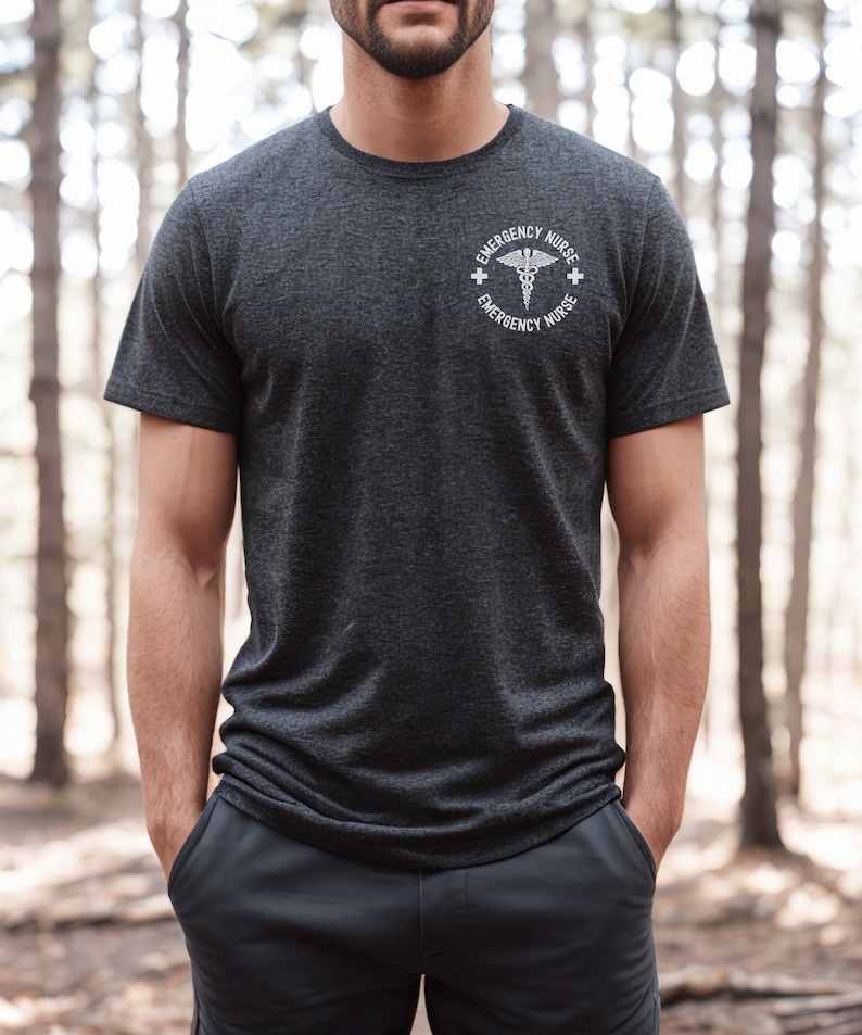 May include: A dark heather grey t-shirt with a white graphic of a medical caduceus symbol and the text "Emergency Nurse" on a circle around the symbol.