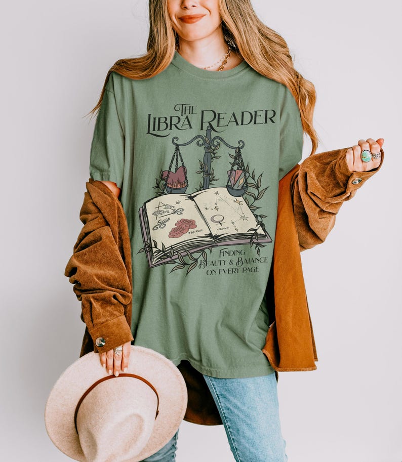 Pu&ograve; includere: Maglietta verde con una grafica di un libro, una bilancia e stelle. Il testo sulla maglietta recita "The Libra Reader" e "Finding Beauty & Balance on Every Page".