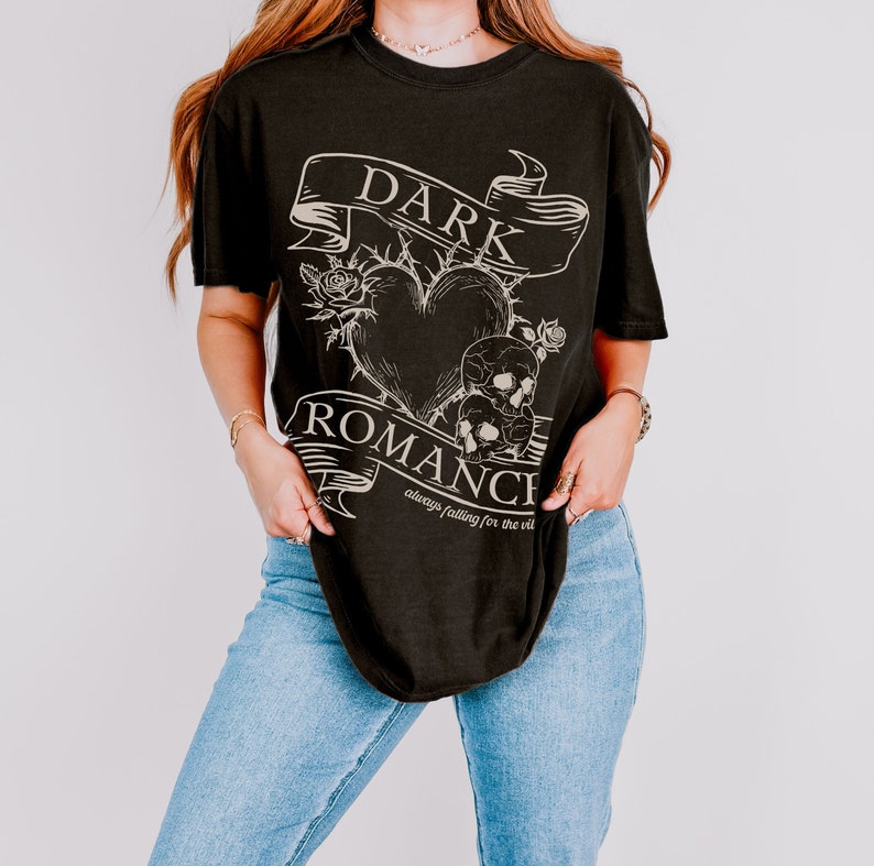 Op de afbeelding: Zwart T-shirt met een grafisch ontwerp van een hart met doornen, schedels en een banner met de tekst "DARK ROMANCE always falling for the vil"