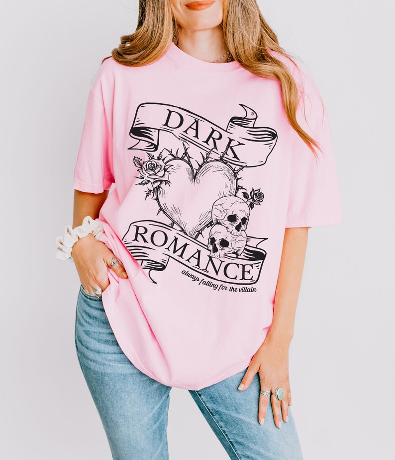 Op de afbeelding: Roze oversized T-shirt met een zwarte grafische print van een hart met doornen, twee schedels en een banner met de tekst "DARK ROMANCE always falling for the villain".