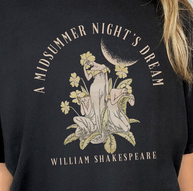 May include: A black t-shirt featuring a white graphic print of three women in a garden setting. The text "A Midsummer Night's Dream" is printed in a circle around the women. The text "William Shakespeare" is printed below the graphic.