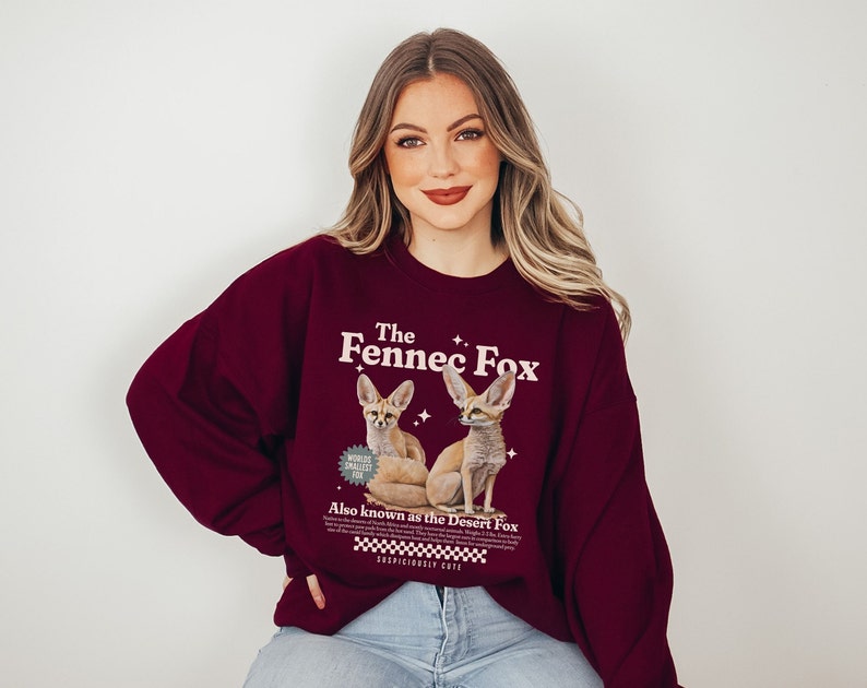 May include: A maroon sweatshirt with a graphic of two fennec foxes. The text on the sweatshirt reads "The Fennec Fox" and "Also known as the Desert Fox".