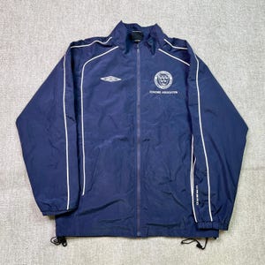 Könnte beinhalten: Marineblaue Reißverschlussjacke mit weißem Paspel und Umbro-Logo. Die Jacke hat ein Coaches Association-Emblem auf der Brust. Die Jacke hat einen durchgehenden Reißverschluss und Kordelzüge am Saum.