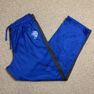 Può includere: Pantaloni della tuta blu con pannelli laterali neri e un logo Rams bianco sulla gamba sinistra. I pantaloni della tuta hanno una cintura con coulisse e un logo Nike sulla gamba destra.