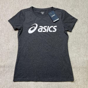 以下が含まれることがあります： 胸に白い「asics」のロゴが入ったチャコールグレーのTシャツ。Tシャツは半袖とクルーネックです。「asics」のロゴが入ったタグが付いています。