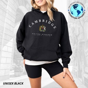 May include: Black unisex hoodie with a white graphic print of the word "CAMBRIDGE" in an arc above a coat of arms and the text "UNITED KINGDOM 51.7520'N 1.2577'W".