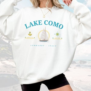 May include: White sweatshirt with a blue and white sailboat graphic and the text "LAKE COMO" in blue. The text "LOMBARDY - ITALY" is printed below the graphic.