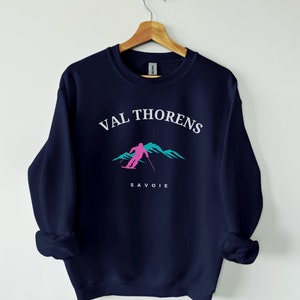 May include: Navy blue sweatshirt with a white graphic of a skier in the mountains. The text "VAL THORENS SAVOIE" is printed on the sweatshirt.