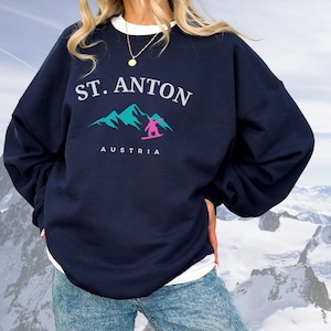 May include: A navy blue sweatshirt with a white graphic print of mountains and a skier. The text "ST. ANTON" and "AUSTRIA" are printed on the sweatshirt.
