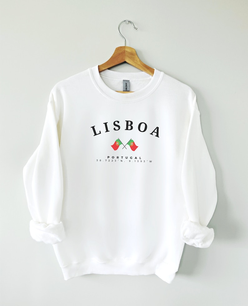 May include: White sweatshirt with black text that reads "LISBOA" and "PORTUGAL" with two crossed Portuguese flags and coordinates "38.7223&deg; N, 9.1393&deg; W".