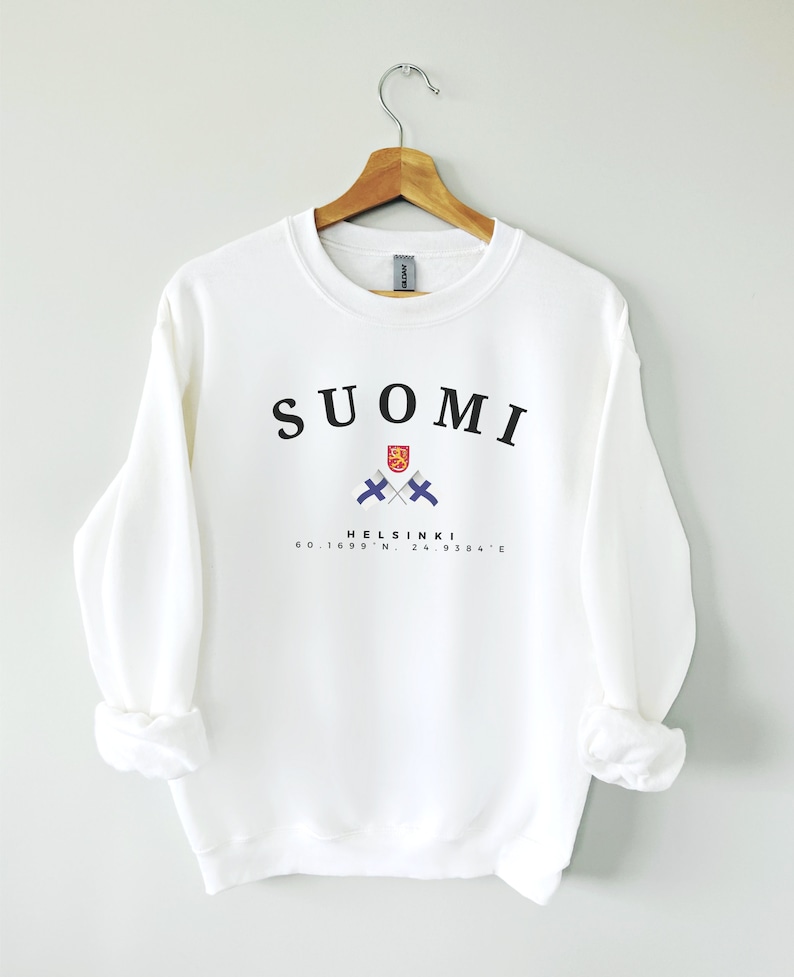 以下が含まれることがあります： 白いスウェットシャツに、黒い文字で「SUOMI」と書いてあり、2つの交差したフィンランドの国旗とフィンランドの国章のグラフィック、そして黒い文字で「HELSINKI 60.1699&deg; N, 24.9384&deg; E」と書いてあります。