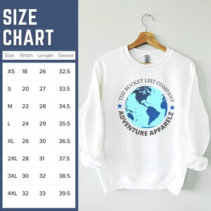 May include: White sweatshirt with a blue and light blue graphic of a globe with the text "The Bucket List Company Adventure Apparelz". A size chart is shown with measurements in inches for XS, S, M, L, XL, 2XL, 3XL, and 4XL.