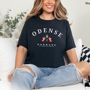 May include: A heather black unisex t-shirt with the text "ODENSE" in white, with two crossed Danish flags and the text "DANMARK 55.4038°N 10.4024°E" underneath.