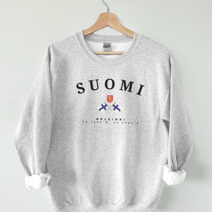 以下が含まれることがあります： グレーのトレーナーに、黒い文字で「SUOMI」と書いてあり、フィンランドの国旗が交差したデザインと、黒い文字で「HELSINKI 60.1699&deg; N, 24.9384&deg; E」と書いてあります。