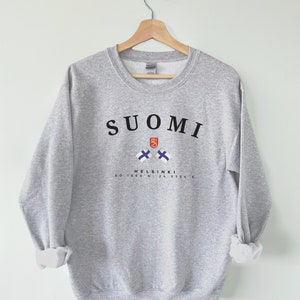 以下が含まれることがあります： グレーのトレーナーに、黒い文字で「SUOMI」と書いてあり、フィンランドの国旗が2つ交差して、黒い文字で「HELSINKI 60.1699&deg; N, 24.9384&deg; E」と書いてあります。