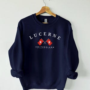 May include: Navy blue sweatshirt with a white graphic of crossed Swiss flags and the text "LUCERNE SWITZERLAND 47.0503° N 8.3087° E"