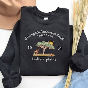 May include: Black sweatshirt with a white graphic design featuring a tree, sun, and animals. The text reads "Serengeti National Park Tanzania 19 51 Endless Plains".