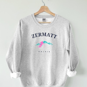 May include: Grey sweatshirt with a blue and white graphic of a skier in the mountains. The text "ZERMATT" and "VALAIS" is printed on the sweatshirt.