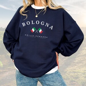 May include: A navy blue sweatshirt with the text "BOLOGNA" in white letters. The sweatshirt also features two crossed Italian flags and the text "EMILIA-ROMAGNA" in white letters.