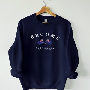 Puede incluir: Sudadera azul marino con texto blanco que dice "BROOME AUSTRALIA 17.9814°S, 122.1358°E" y dos banderas australianas cruzadas.