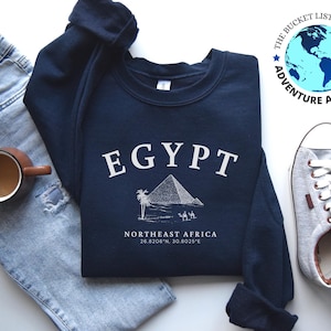 May include: A navy blue sweatshirt with a white graphic of a pyramid and the text "EGYPT" and "NORTHEAST AFRICA 26.8206°N, 30.8025°E".