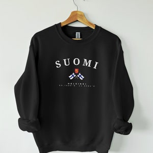 以下が含まれることがあります： 白い文字で「SUOMI」と「HELSINKI」と座標「60.1699&deg; N, 24.9384&deg; E」が書かれた黒いスウェットシャツ。スウェットシャツには、交差したフィンランドの国旗も描かれている。