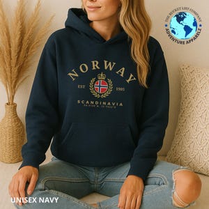 Peut inclure: Sweat à capuche bleu marine avec une poche avant et une capuche. Le sweat à capuche porte le mot "NORWAY" en lettres dorées, ainsi qu'un écusson et le texte "SCANDINAVIA". Le bas du sweat à capuche indique "UNISEX NAVY".