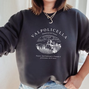 Puede incluir: Sudadera negra con un diseño gráfico blanco con el texto "Valpolicella Innamorati del Veneto" y un dibujo de un viñedo con un castillo en el fondo. El texto debajo del gráfico dice "Negrar, Sant'Ambrogio e Fumane ti porteranno via il cuore."
